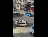 Blue car drives on sidewalk to pass trucks blocking road 