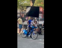 Man balances tv while on bike at park