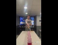 Guy throws ball into lined up cups 