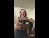 Girl holds small cardboard box with white black cat in it 