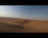 Guy snowboards down desert sand dune and falls into sand