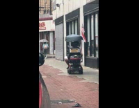 Guy rides mobile scooter with tent and flags 