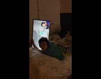 Kid laying in bed holding monitor sideways watching stream