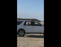 White SUV car making donuts in the dirt on an empty lot 
