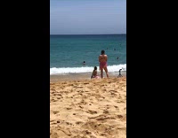 Woman in bikini kneels while beach waves hit her