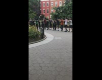 People wearing blindfolds walk in single file line with hands on shoulders in the park