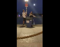 Woman poses with flower in front of trash bin