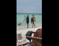 Blonde girl black dress hold tripod beach