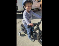 Boy sitting on bike with training wheels sticks tongue out 