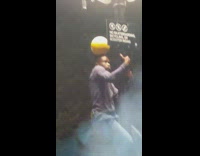 Guy climbs up lamppost while balancing ball on head at night 