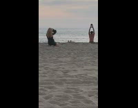 Shirtless guy lifts kettlebell beach orange sky 