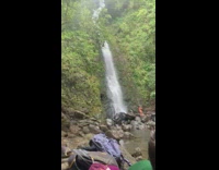 Woman in orange braids kneels beside the waterfalls