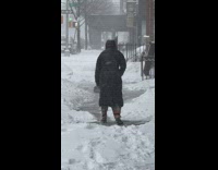 Guy on sidewalk shoveling snow with a dust pan 
