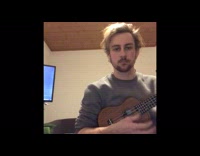 Guy wearing grey sweater plays the ukulele 