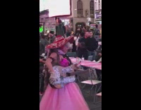 Woman pink dress holds Chik fil a cup, sings and plays guitar on street