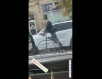 Guy rides high wheel bicycle top hat 