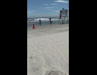 Girl kneels beach shore white lifeguard tower 