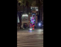 Guy wearing glowing light outfit rides scooter