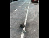 Hole in the middle of the road with smoke coming out of the hole 
