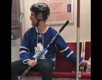 Guy in blue hockey jersey and hockey stick pours water on his face  on subway train