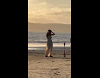 Woman in white outfit tiktok dance at the beach at sunset