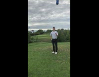 Guy tees off and hits golf ball, shotguns blue beer can on golf course, then friend spits out golf ball out of mouth