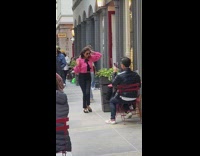 Woman in Pink Jacket Dances next to Red Table with Drink 