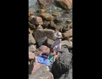 Woman in white beach dress poses on the beach rocks