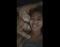woman in striped shirt cuddles with orange cat