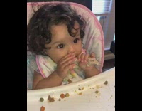 Little curly haired baby girl eating entire chicken drumstick leg