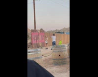 Blonde Lady Wearing Hat Swings Purse in Front of Fence 