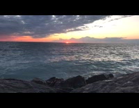 Waves crash black rocks sunset pink sky 