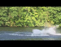 Man red blue wetsuit spins in mid air and backflips on blue jet ski multiple times in lake water