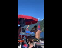 Two men holds out a banana and a bun at the beach