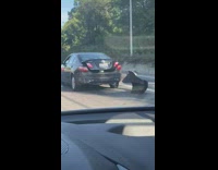 Black car dragging broken rear bumper on freeway