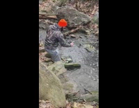 Man poses underneath a rock on a creek 