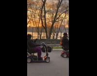 Two people ride mobility wheelchair scooter park 