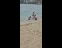 Woman in bikini kneels and reached by waves twice