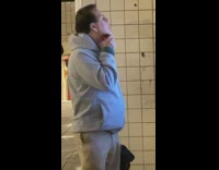 Man shaves his face with shaver while looking at sign in subway station 