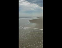 Person standing in shallow waves gets knocked down at beach