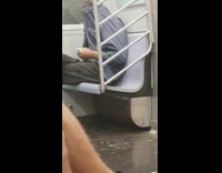 Man puts box of cigarettes in shirt pocket with shirt buttoned over his face on subway train