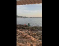 Woman in green dress poses at the rocky beach shore