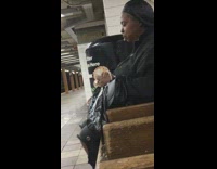 Woman black silk head scarf closes eyes and chews food on bench with food on chin, subway station