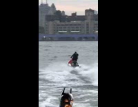 Batman with cape drives away on jet ski on harbor
