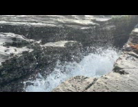 Waves splashes upward from the rocks at shore 