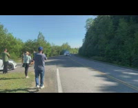 Spectators standing on side of road watching a car doing a burnout