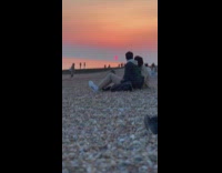 Couple sit down on rocky beach sunset 