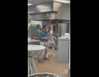 Woman in beige dress dances with a man inside the kitchen
