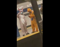 Two people in cartoon onesies wait for train 