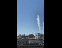 Airplane jets stream over white building into city